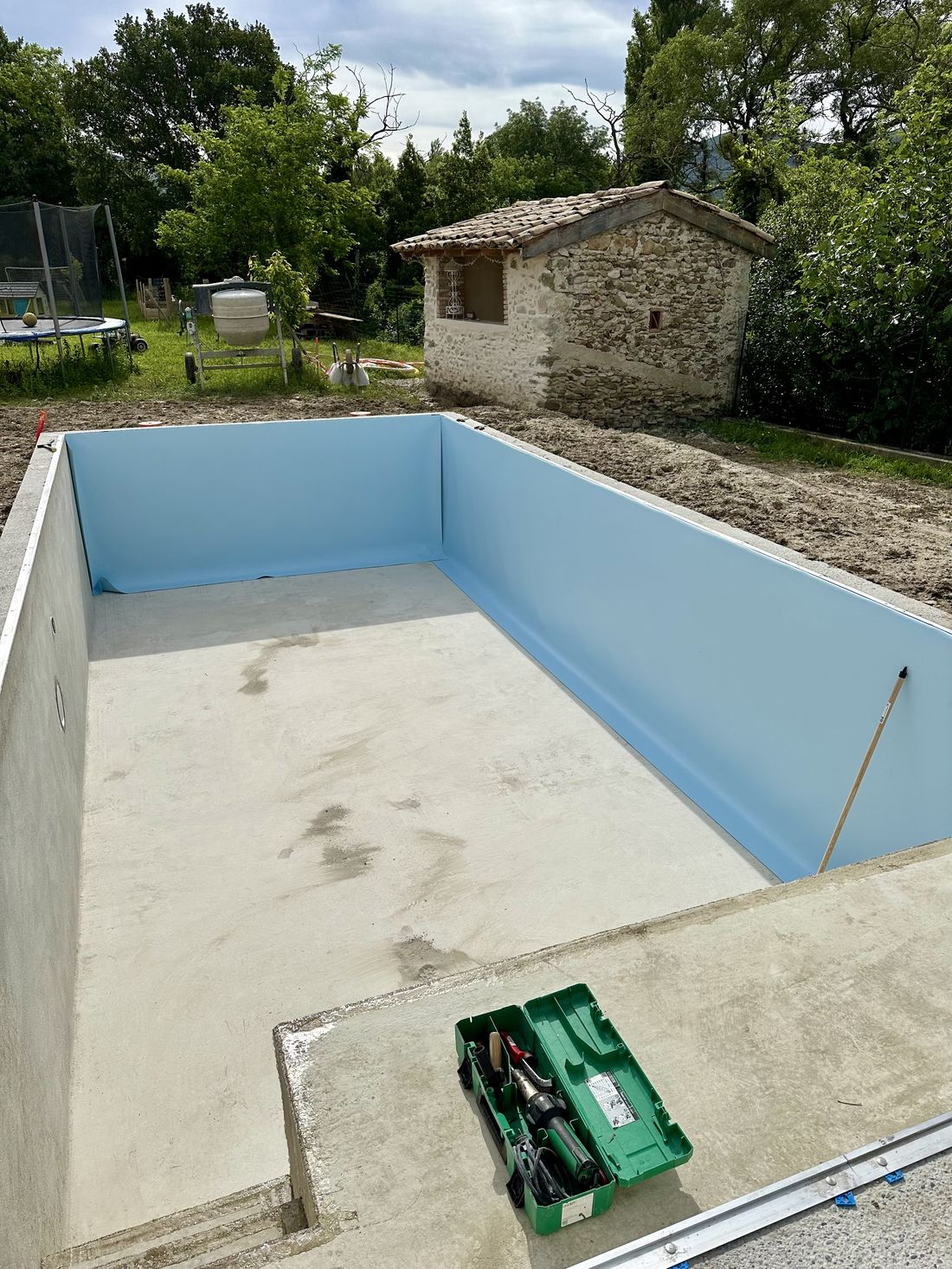 Bassin en cours de pose, membrane bleu clair, outillage sur la margelle